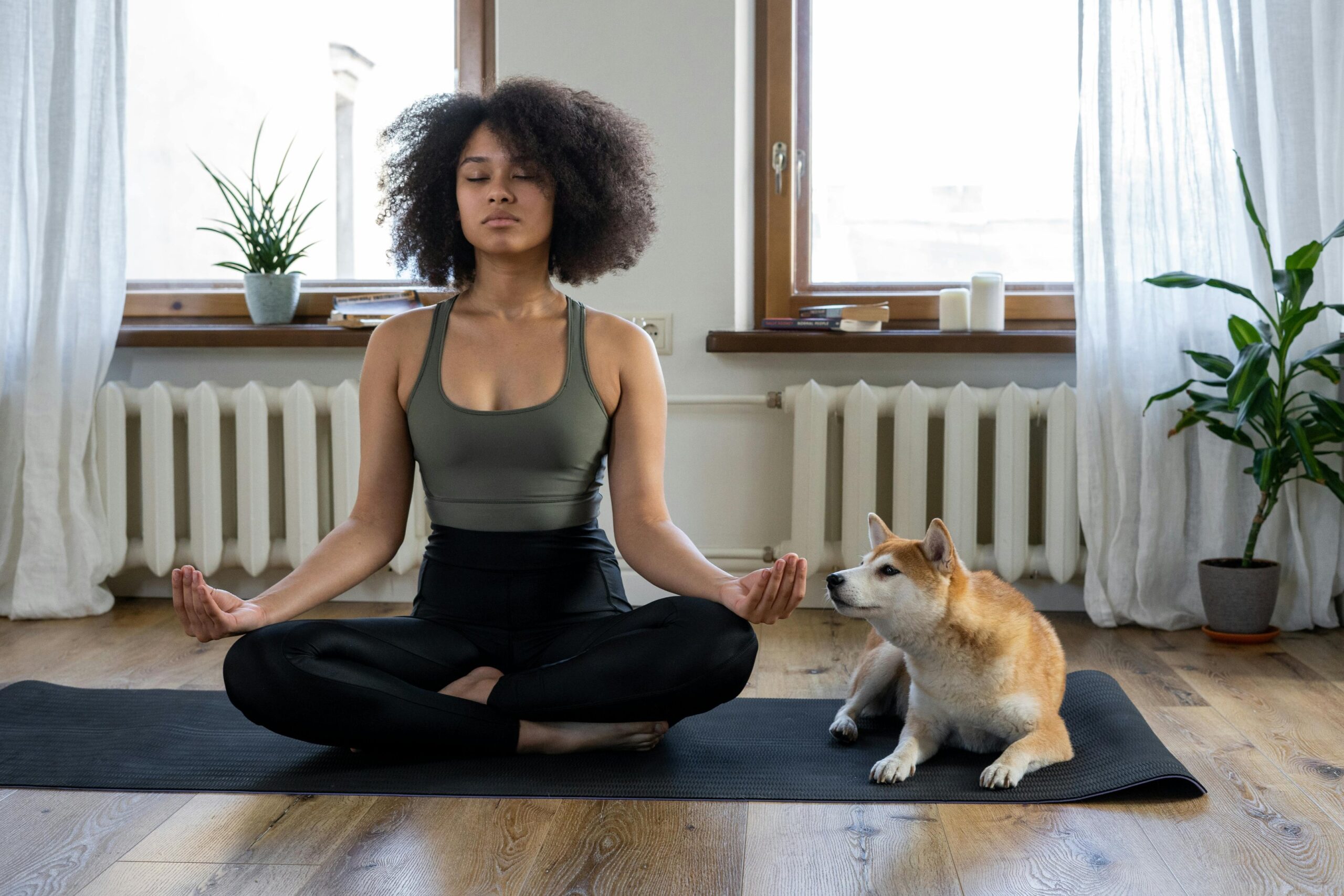 A woman doing yoga on a mat at home with her dog